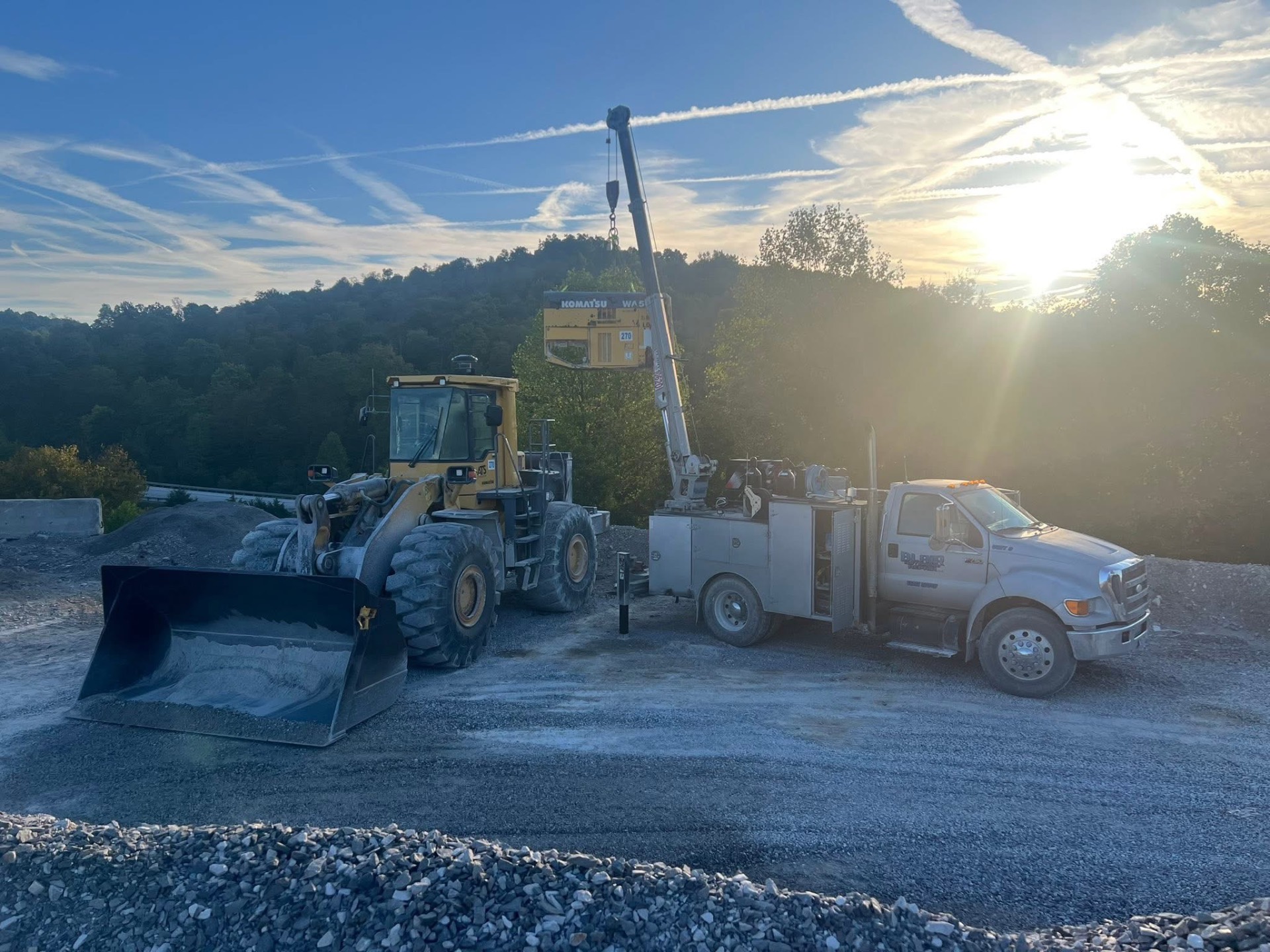 Service truck lifting Komatsu wheel loader components at sunrise
